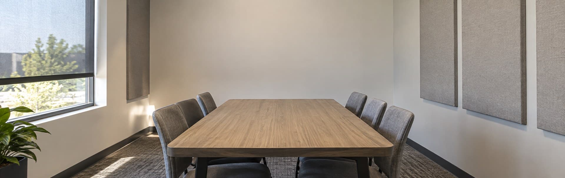 Small meeting room with a table, chairs, acoustic panels, and a blank front wall